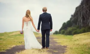 Un couple de jeunes mariés se promène main dans la main sur un chemin, un bouquet à la main. Un beau mariage au mois de mai.