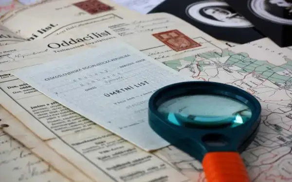 Loupe pour retrouver un acte de décès. Documents anciens, carte et loupe suggèrent une recherche généalogique.